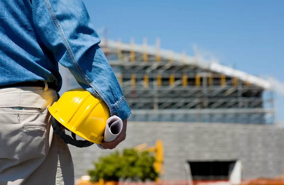 A man in blue jeans and a hard hat holding a yellow helmet, ready for security needs assessment to improve building safety